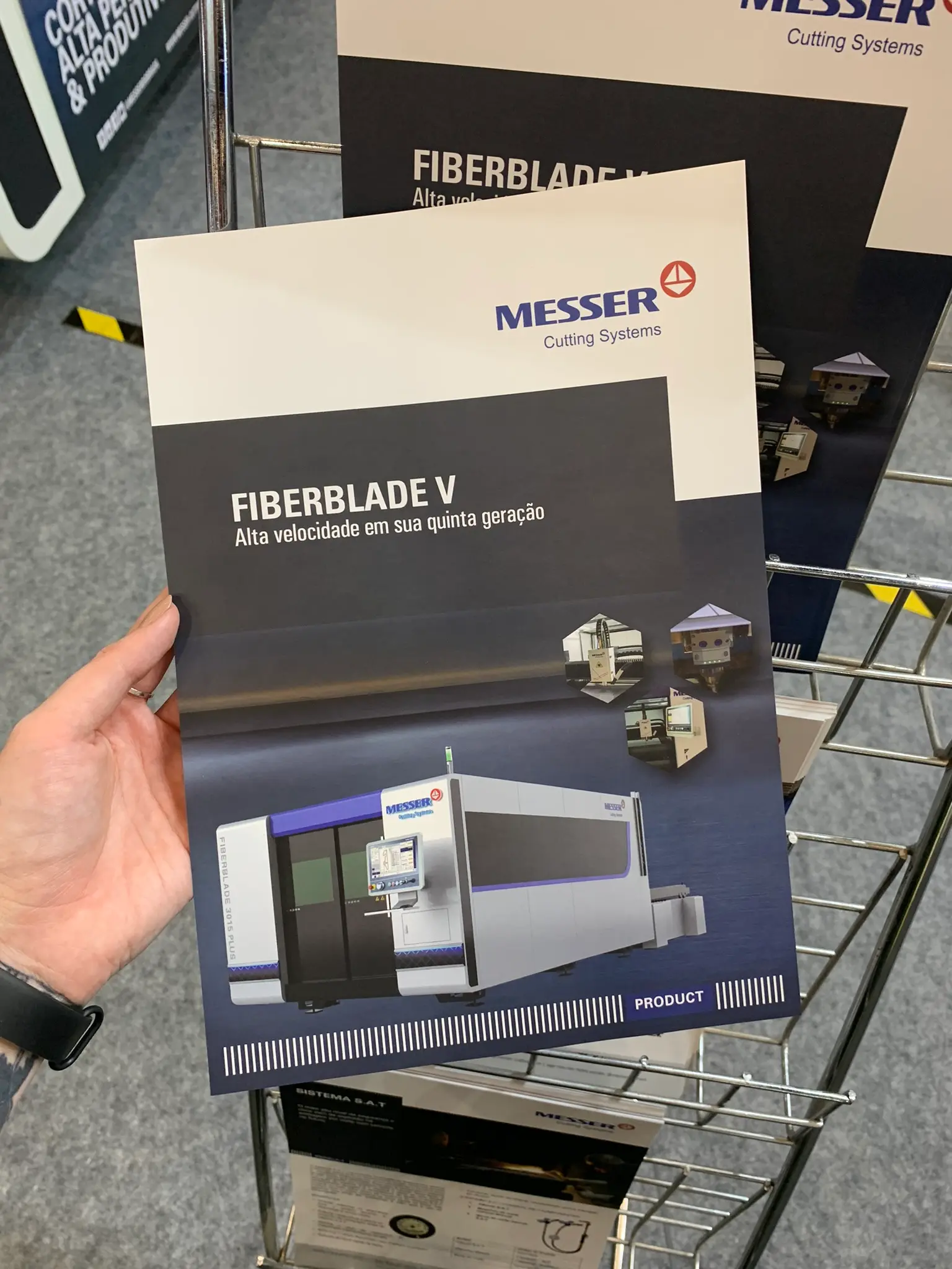 Folheto FiberBlade V na mão de um visitante, em frente à máquina